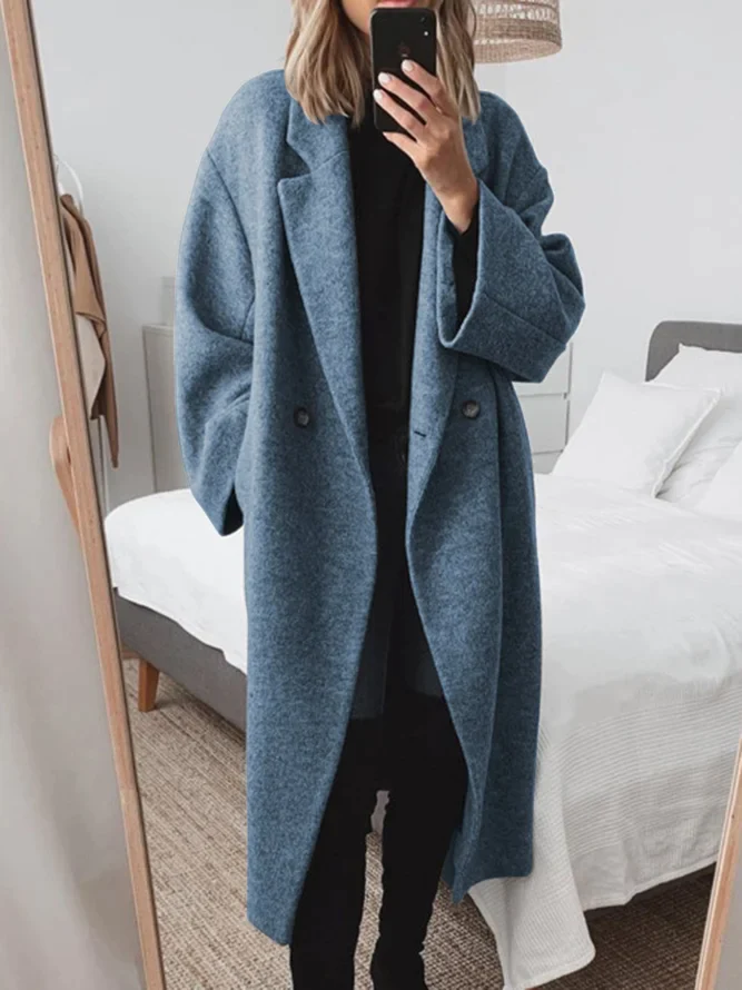 Donna in cappotto oversize blu scuro, scatta selfie allo specchio in camera da letto moderna. Moda autunnale, abbigliamento casual elegante.