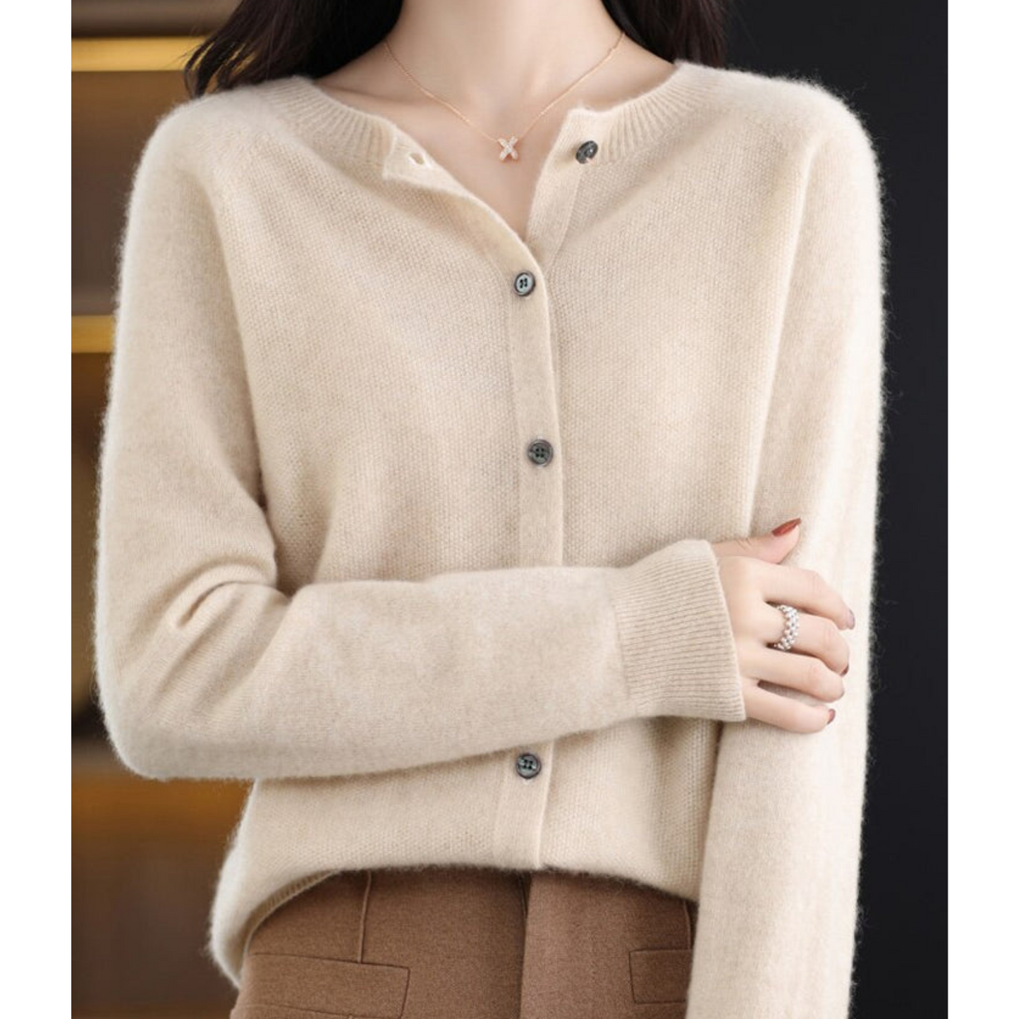 Donna indossa cardigan beige in cashmere con bottoni, abbinato a pantaloni marroni. Look elegante e caldo per l'autunno. Moda femminile chic.