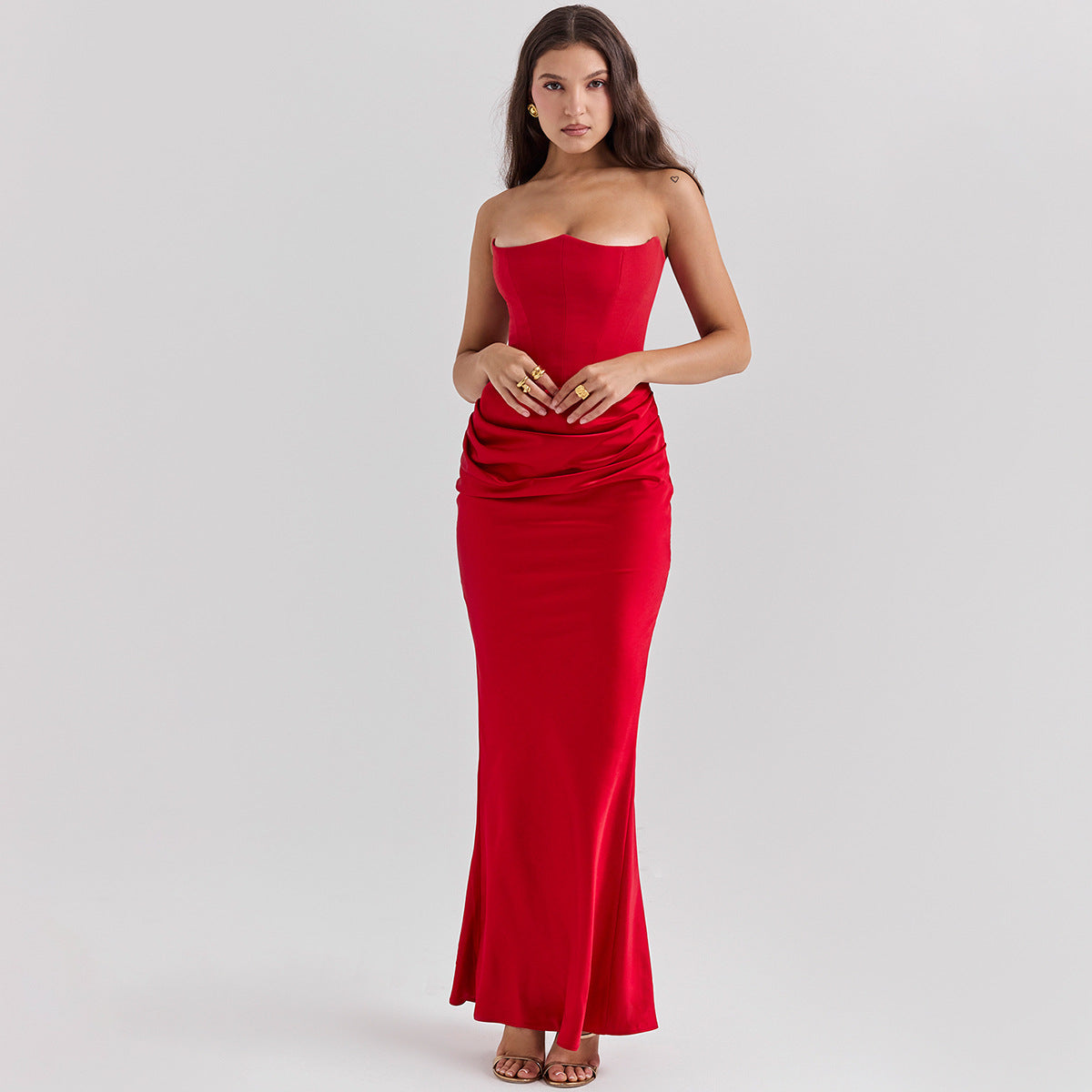 Donna in abito lungo rosso elegante, senza spalline, con drappeggio in vita, posa su sfondo neutro. Moda femminile, abbigliamento da sera.