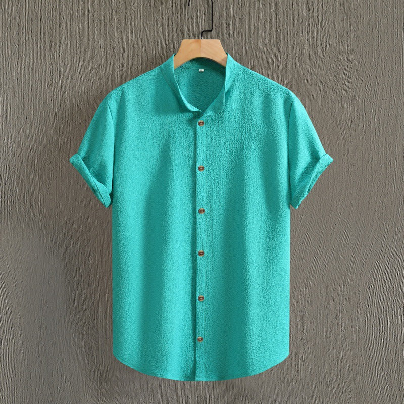 Camicia verde acqua a maniche corte, tessuto leggero, colletto alla coreana, bottoni in legno, appesa su gruccia. Moda estiva casual uomo.