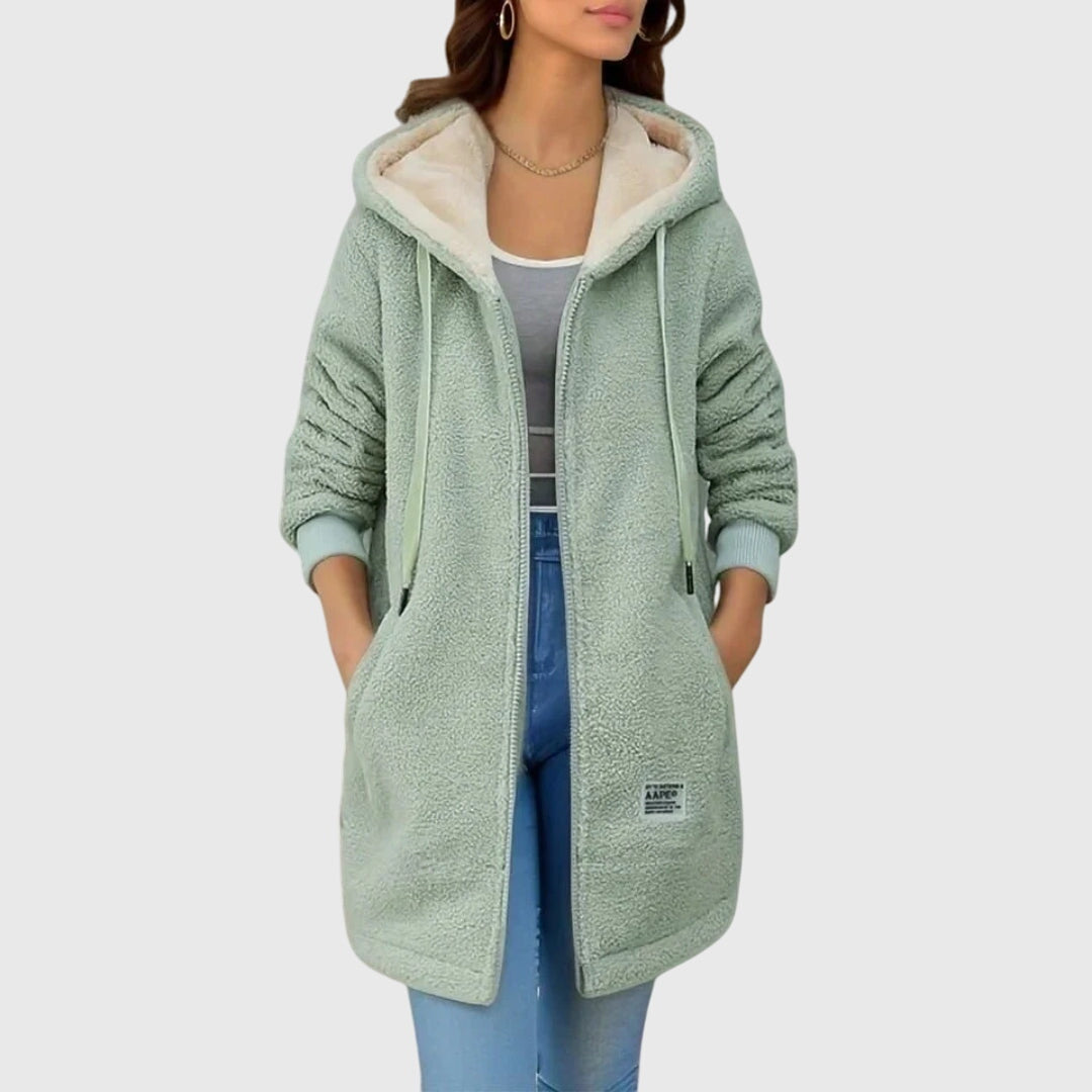 Donna con cappotto in pile verde menta, cappuccio e tasche, indossa jeans e top grigio. Moda autunnale, abbigliamento casual, stile confortevole.