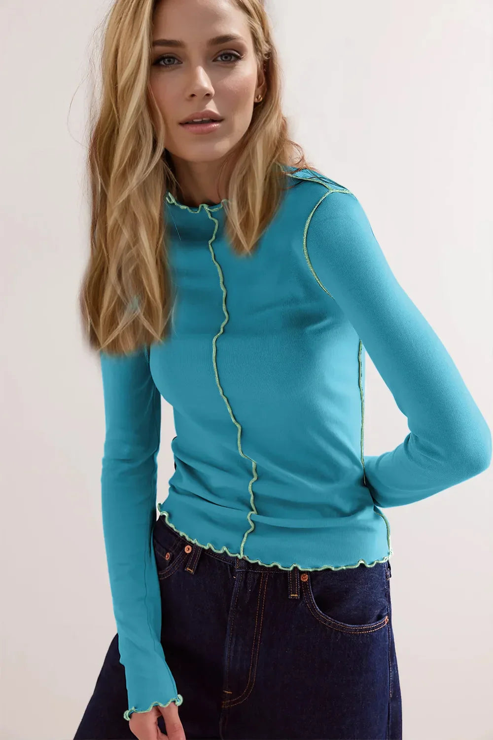 Donna con maglia azzurra a maniche lunghe e jeans scuri. Stile casual, moda femminile, abbigliamento autunnale. Sfondo neutro.