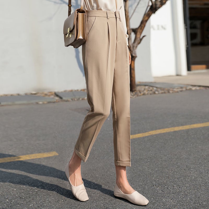 Pantaloni beige eleganti da donna, abbinati a scarpe basse e borsa a tracolla marrone chiaro, su sfondo urbano. Moda femminile casual chic.