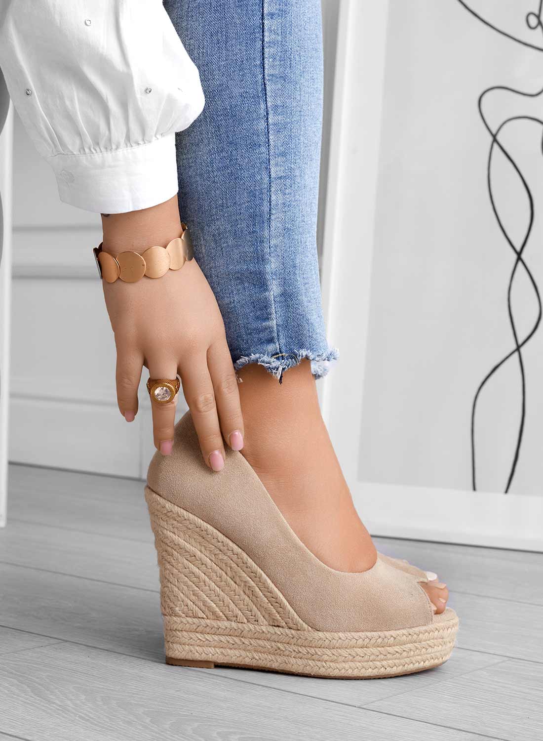 Donna indossa scarpe con zeppa beige, jeans strappati, camicia bianca, bracciale dorato e anello con pietra. Moda casual elegante.