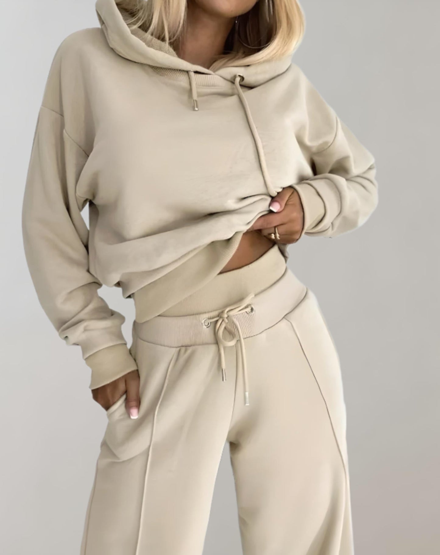 Donna in tuta beige, felpa con cappuccio e pantaloni coordinati. Moda casual, abbigliamento comodo, stile minimalista, tendenza autunnale.
