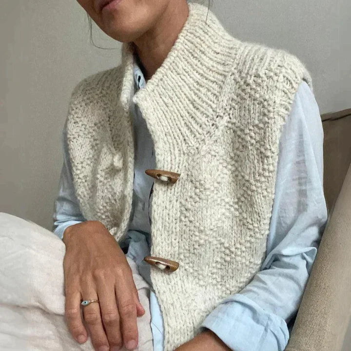 Gilet in maglia beige con bottoni in legno, indossato su camicia azzurra. Moda autunnale, abbigliamento casual elegante, stile artigianale.