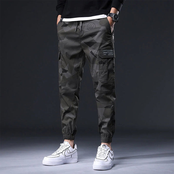Pantaloni cargo mimetici da uomo, stile casual, con tasche laterali, indossati con sneakers bianche Nike. Moda streetwear moderna.