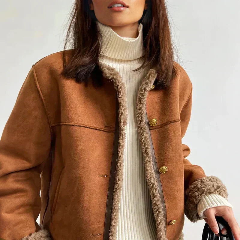 Giacca invernale marrone con bottoni dorati e interno in pelliccia sintetica, indossata su maglione a collo alto bianco. Moda autunnale donna.