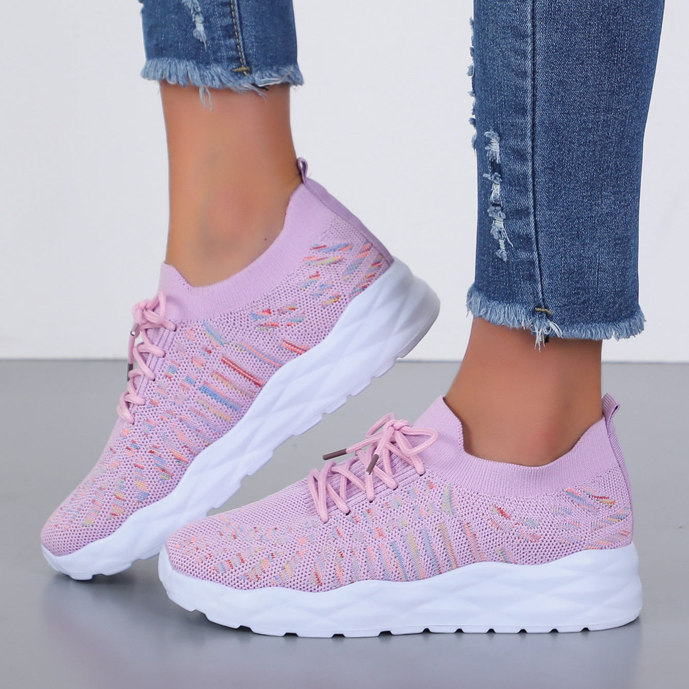Scarpe da ginnastica rosa in maglia traspirante, suola bianca spessa, indossate con jeans strappati. Scarpe sportive moda donna, comode e leggere.