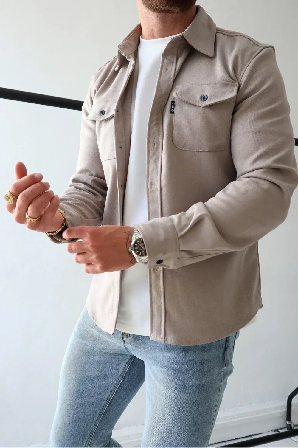 Uomo in camicia beige e jeans, indossa orologio e anelli d'oro. Moda casual maschile, stile moderno, abbigliamento autunnale.