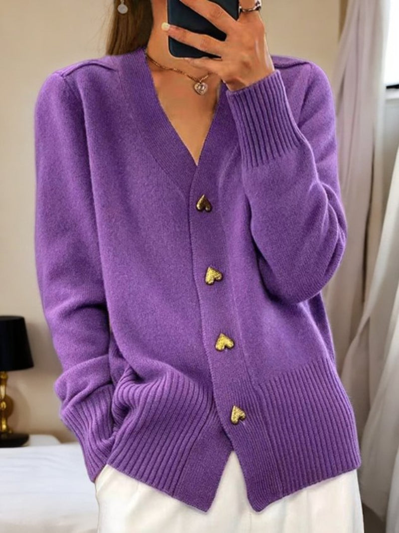 Donna indossa cardigan viola con bottoni a forma di cuore, abbinato a pantaloni bianchi. Stile casual elegante, moda autunnale femminile.