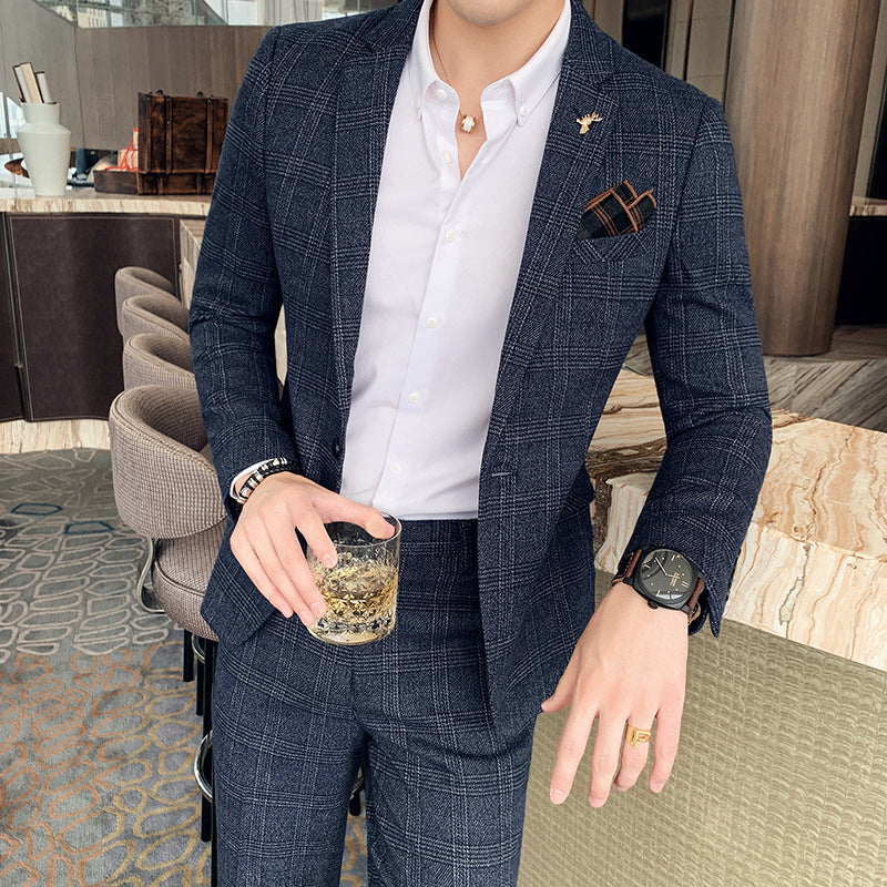 Uomo in elegante abito a quadri blu, camicia bianca, orologio nero, anello dorato, tiene bicchiere di whisky. Moda maschile, stile sofisticato.