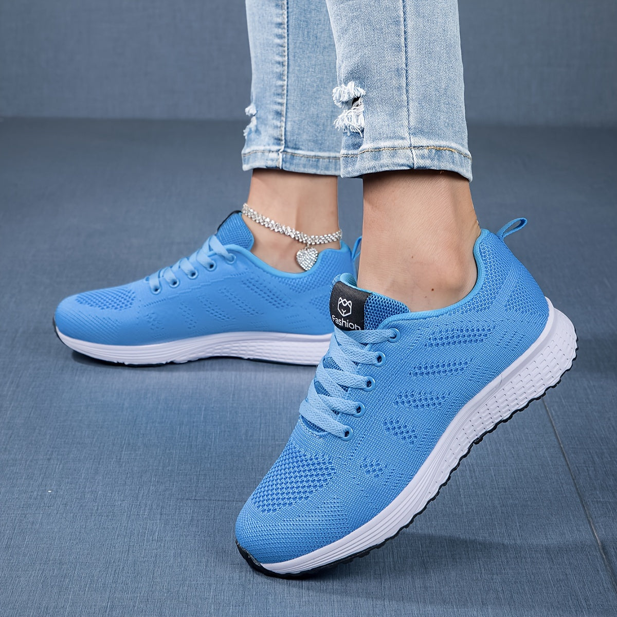 Scarpe da ginnastica blu da donna su sfondo blu, indossate con jeans strappati. Scarpe sportive leggere, suola bianca, design moderno.