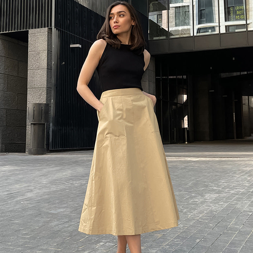 Donna in abito elegante nero e gonna beige, posa urbana. Moda femminile, outfit chic, stile contemporaneo. Sfondo architettonico moderno.