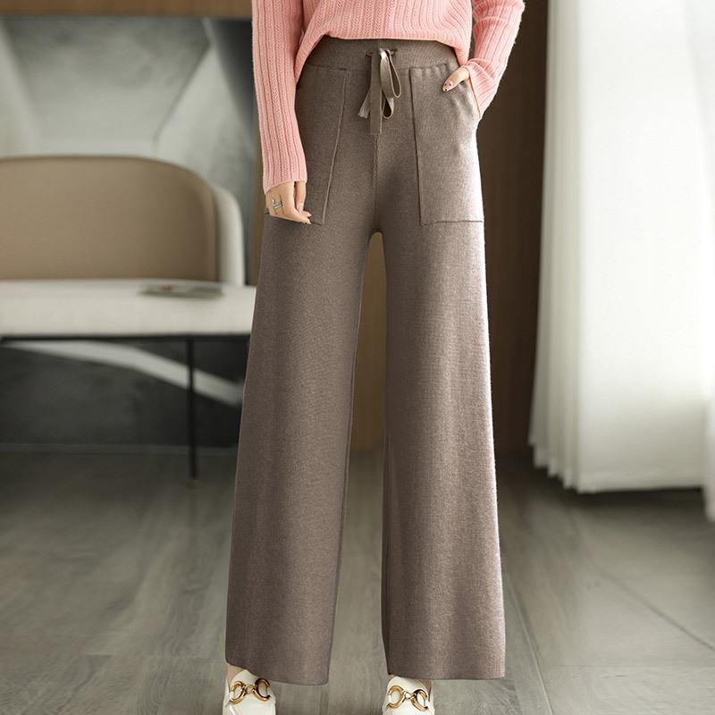 Donna in pantaloni larghi marroni e maglione rosa, in piedi in un salotto moderno. Moda autunnale, abbigliamento casual elegante.