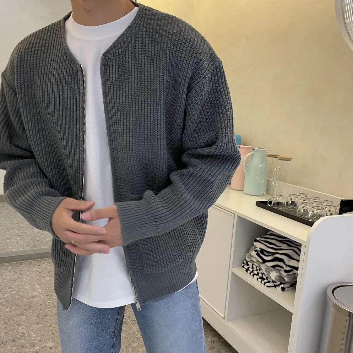 Uomo con cardigan grigio a maglia, t-shirt bianca e jeans, in cucina moderna con scaffale bianco e stoviglie. Moda casual autunnale.