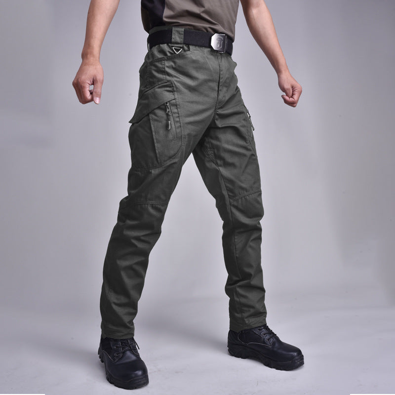 Pantaloni cargo tattici verde militare, uomo in piedi, tasche multiple, cintura nera, scarpe nere, abbigliamento outdoor resistente e funzionale.