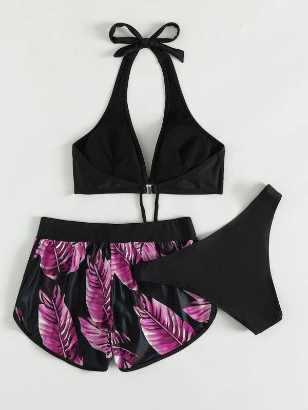 Bikini nero con top a triangolo e slip, abbinato a shorts con stampa foglie rosa. Moda mare donna, costumi da bagno estivi eleganti.
