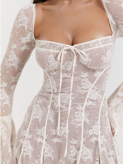 Abito in pizzo bianco trasparente con dettagli floreali, maniche lunghe e scollo quadrato. Elegante e femminile, perfetto per eventi speciali.