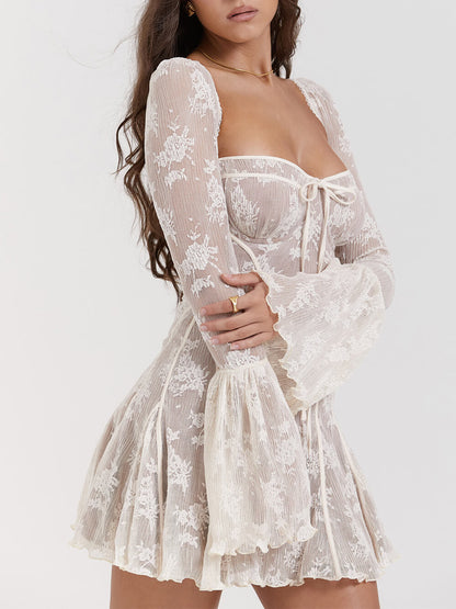 Abito corto in pizzo bianco con maniche lunghe svasate e dettagli floreali, indossato da una donna. Elegante e femminile, perfetto per eventi speciali.