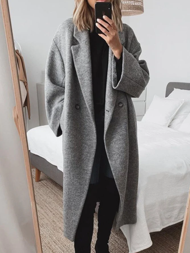 Donna in cappotto grigio oversize scatta selfie in camera da letto moderna; moda autunnale, abbigliamento casual chic, tendenze 2023.