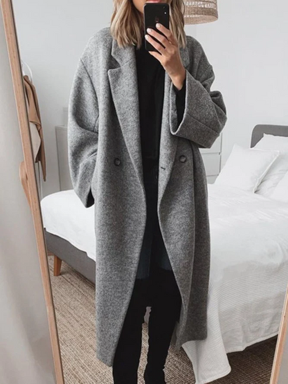 Donna in cappotto grigio oversize scatta selfie in camera da letto moderna. Moda autunnale, abbigliamento casual elegante, specchio a figura intera.