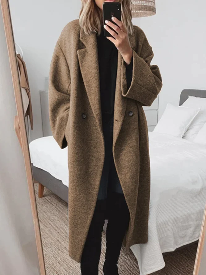 Donna in cappotto oversize marrone scatta selfie in camera da letto moderna. Moda autunnale, abbigliamento casual elegante, tendenze cappotti 2023.