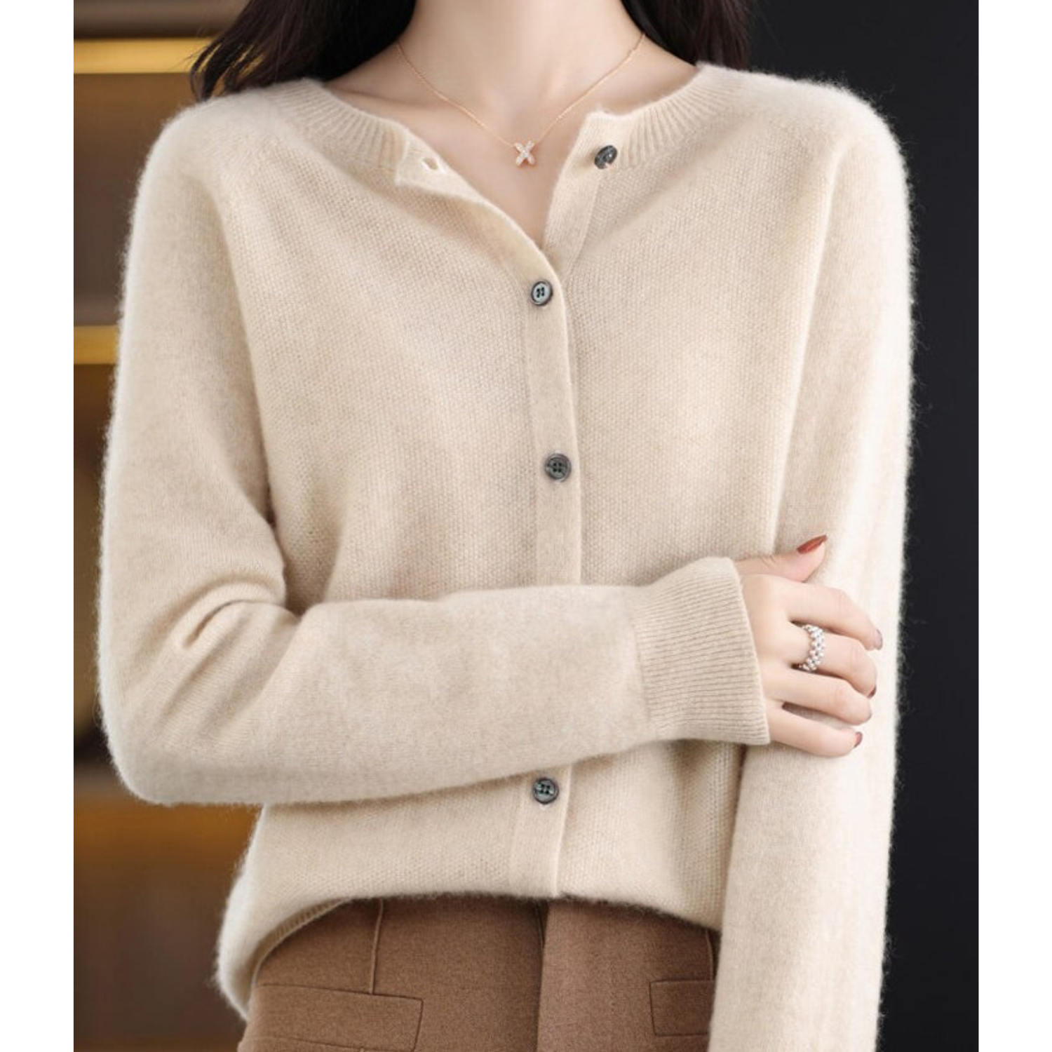 Donna indossa cardigan beige in cashmere con bottoni, abbinato a pantaloni marroni. Look elegante e caldo per l'autunno. Moda femminile chic.