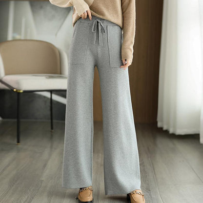 Pantaloni grigi larghi da donna, stile casual, con tasche frontali e laccio in vita, indossati con maglione beige e mocassini marroni.