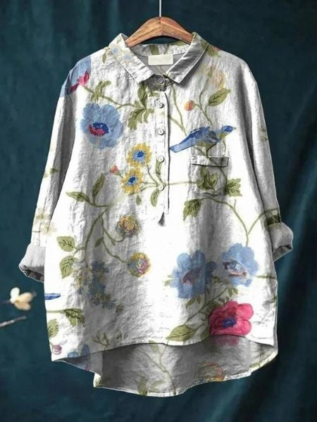 Camicia di lino grigia con stampa floreale colorata e uccelli, maniche lunghe, colletto classico, sfondo blu. Moda donna, abbigliamento casual elegante.