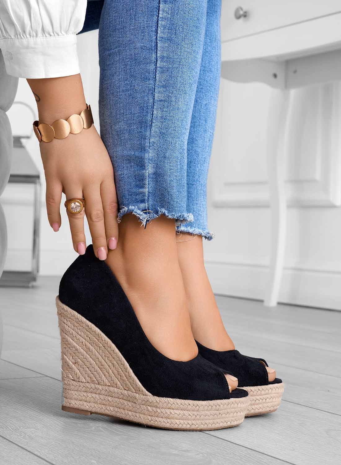 Scarpe con zeppa nere in camoscio, indossate con jeans aderenti. Dettaglio di bracciale dorato e anello. Moda donna, calzature eleganti.