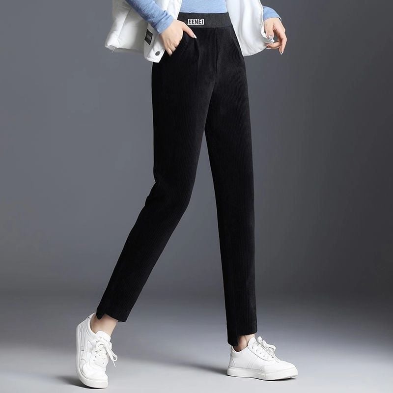 Pantaloni neri a vita alta in velluto a coste, indossati con sneakers bianche e giacca chiara. Moda casual donna, abbigliamento autunnale elegante.