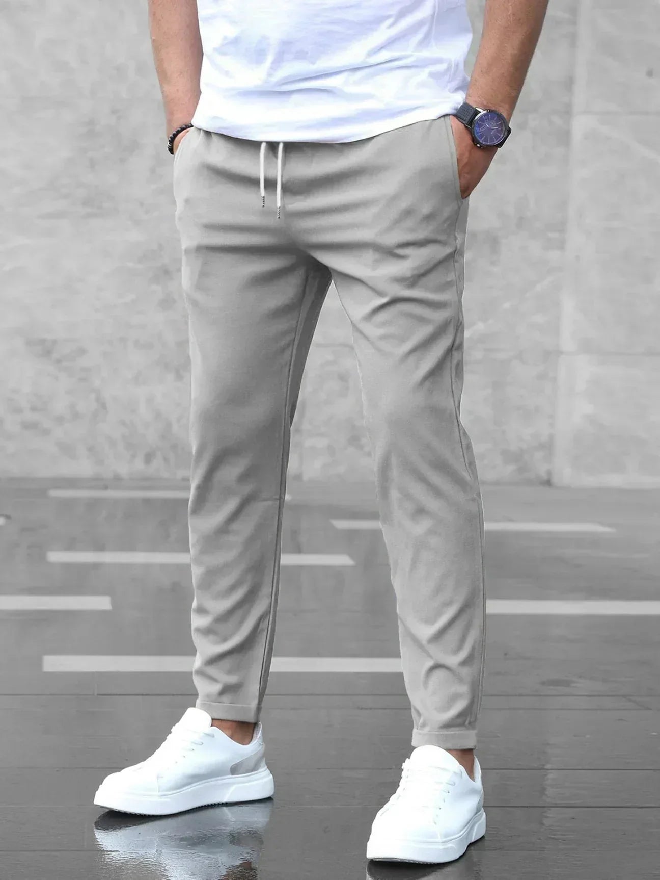 Uomo con pantaloni jogger grigi, t-shirt bianca e scarpe da ginnastica bianche su sfondo grigio. Moda casual maschile, abbigliamento sportivo elegante.