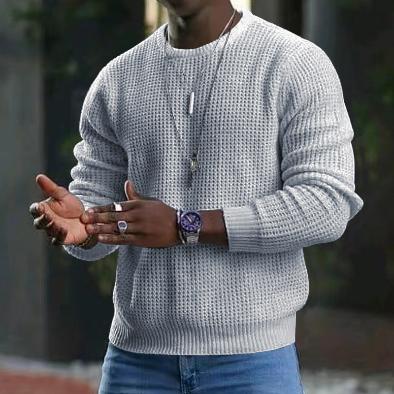 Uomo con maglione grigio a maglia, orologio elegante e collana, sfondo urbano sfocato. Moda maschile autunnale, stile casual chic.