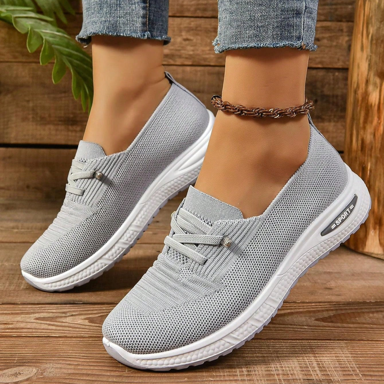 Scarpe da ginnastica grigie in tessuto traspirante, suola bianca, indossate con jeans. Design casual e moderno, ideali per passeggiate e attività quotidiane.