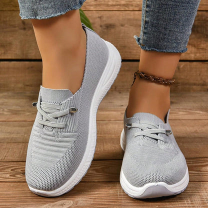 Scarpe da ginnastica grigie da donna, tessuto traspirante, suola bianca, indossate con jeans. Calzature casual comode per passeggiate e sport.