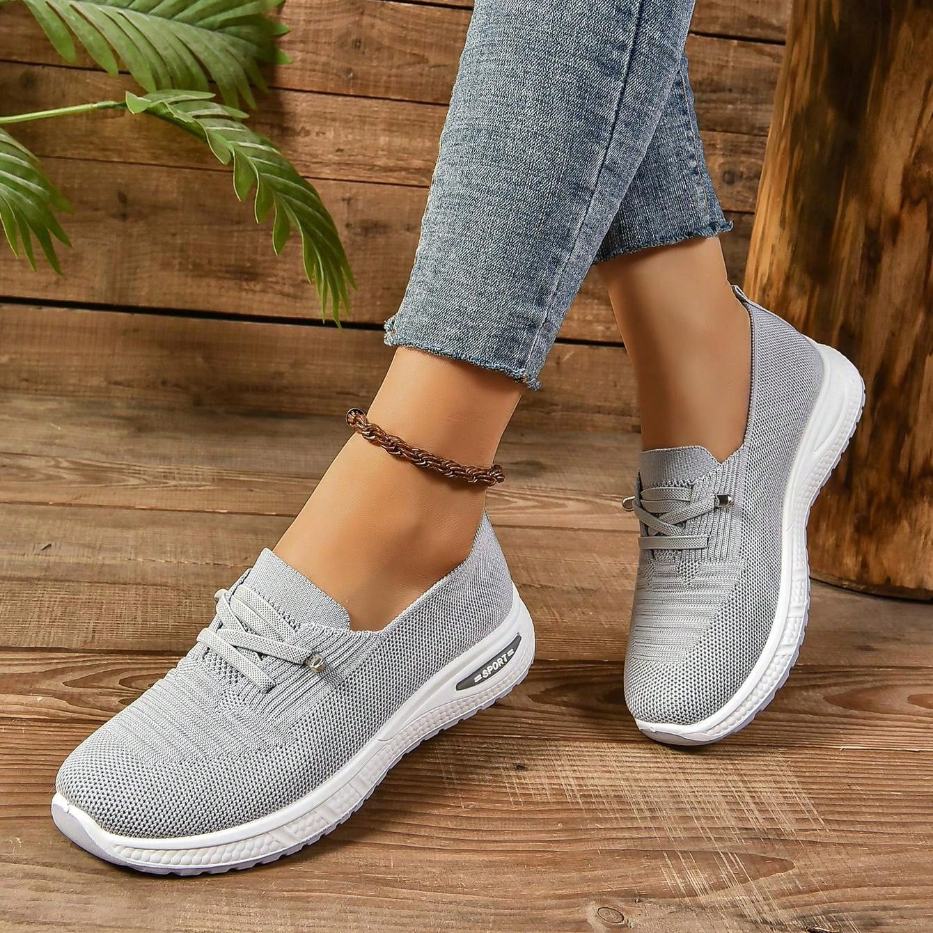 Scarpe da ginnastica grigie da donna, design moderno e traspirante, suola bianca ammortizzata, indossate con jeans su pavimento in legno.