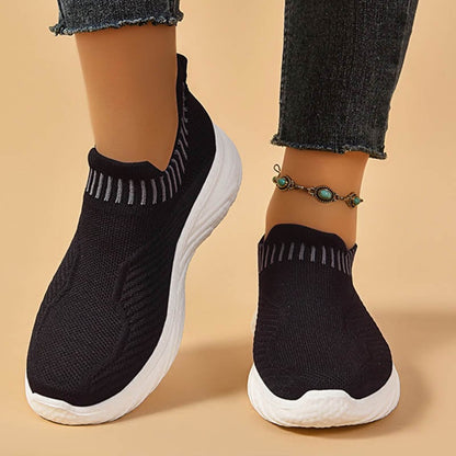 Scarpe da ginnastica nere senza lacci con suola bianca, indossate con jeans e cavigliera verde. Scarpe sportive comode e alla moda.