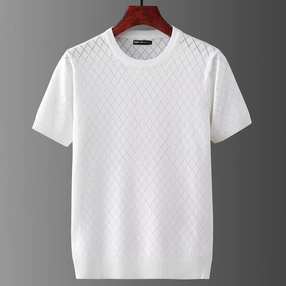 Maglietta bianca a maniche corte con motivo a rombi, appesa su gruccia di legno. Design elegante, ideale per moda estiva casual.