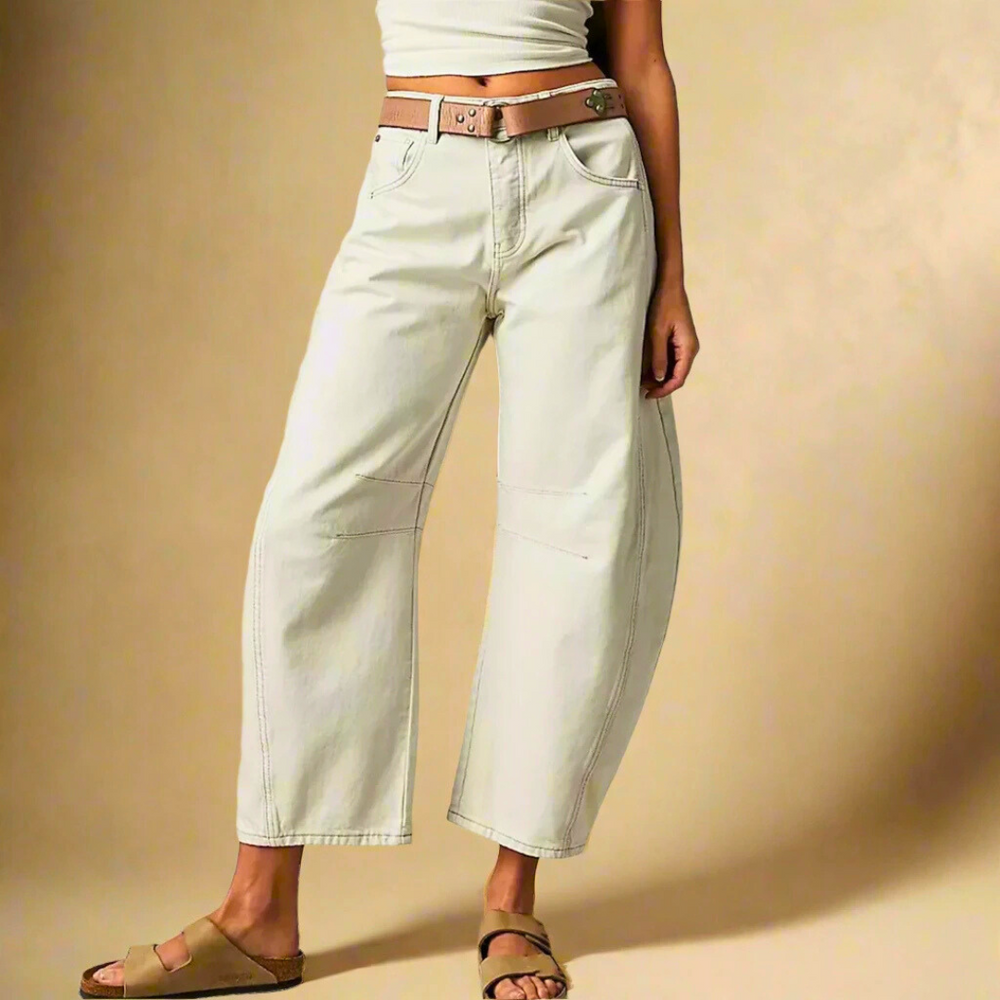 Donna in pantaloni bianchi larghi, cintura marrone, sandali beige. Moda casual, abbigliamento estivo, stile rilassato. Sfondo beige.