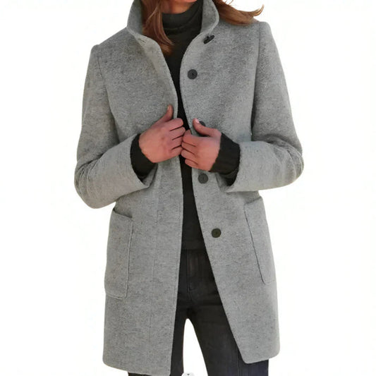 Cappotto grigio donna elegante, invernale, con bottoni neri e tasche frontali, indossato su maglione scuro. Moda femminile autunno inverno.