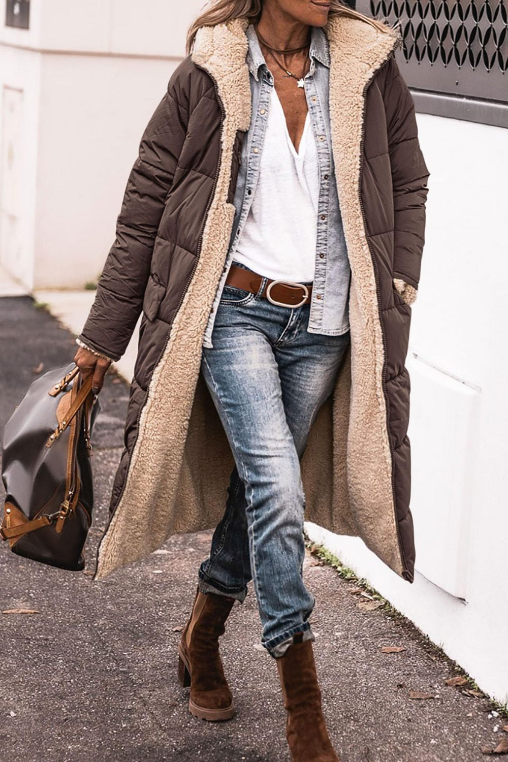 Donna con cappotto lungo marrone imbottito, jeans, stivali marroni e borsa in pelle. Moda invernale casual chic, look urbano elegante.