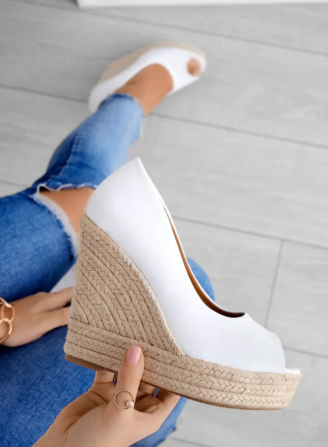 Donna con jeans strappati indossa zeppe bianche in pelle con suola in corda. Scarpe estive eleganti, moda casual, calzature comode.