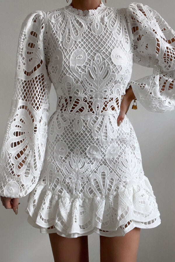 Abito bianco in pizzo con maniche lunghe a sbuffo, dettagli traforati e motivo floreale, ideale per cerimonie eleganti e moda femminile.