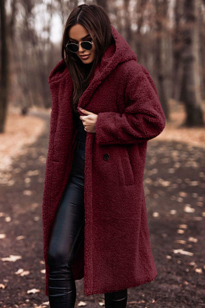 Donna con cappotto lungo in pelliccia sintetica bordeaux, occhiali da sole, pantaloni neri in pelle, passeggia in un parco autunnale. Moda autunno inverno.
