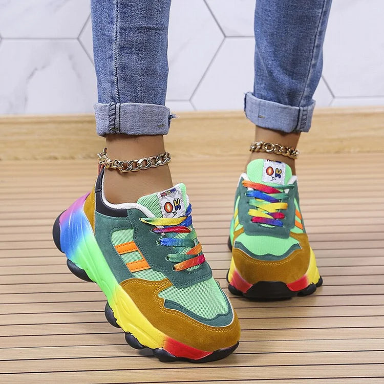 Scarpe da ginnastica multicolore su pavimento in legno, indossate con jeans. Design arcobaleno, suola spessa, dettagli vivaci. Moda casual e trendy.