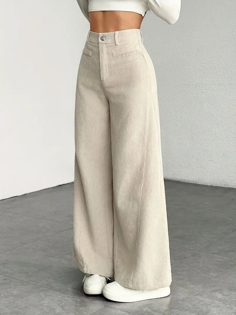 Pantaloni a zampa beige in velluto a coste, moda donna, abbinati a top corto bianco, stile casual chic, pavimento grigio.