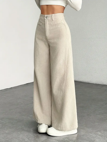 Pantaloni a zampa beige in velluto a coste, moda donna, abbinati a top corto bianco, stile casual chic, pavimento grigio.