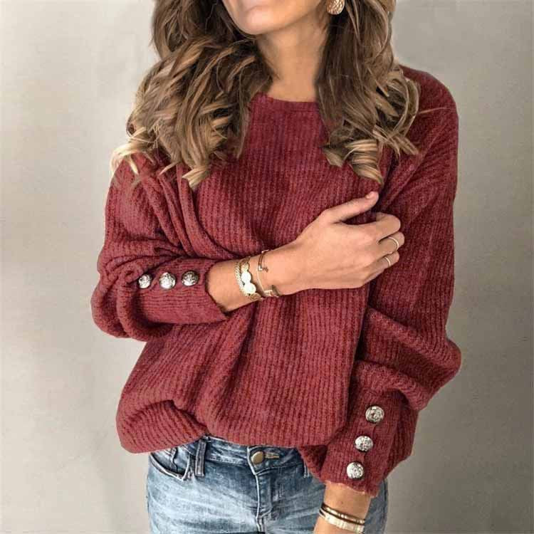 Donna con maglione rosso a coste, bottoni decorativi sulle maniche, indossa jeans e gioielli dorati. Moda autunnale casual elegante.