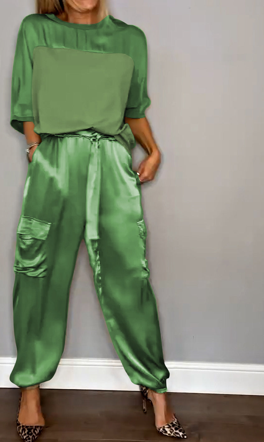 Donna in abbigliamento elegante verde, indossa pantaloni di seta con tasche e top coordinato, scarpe con tacco leopardate. Moda femminile chic.